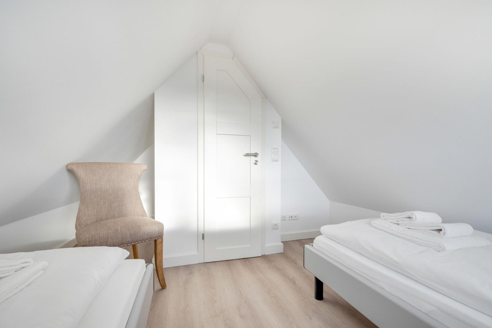 Zimmer mit zwei Betten, Stuhl und Tür unter Dachschrägen.