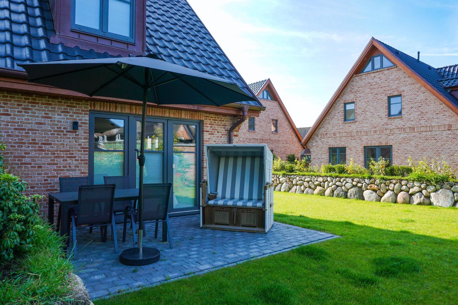 Terrasse mit Tisch, Stühlen und Sonnenschirm neben Strandkorb.