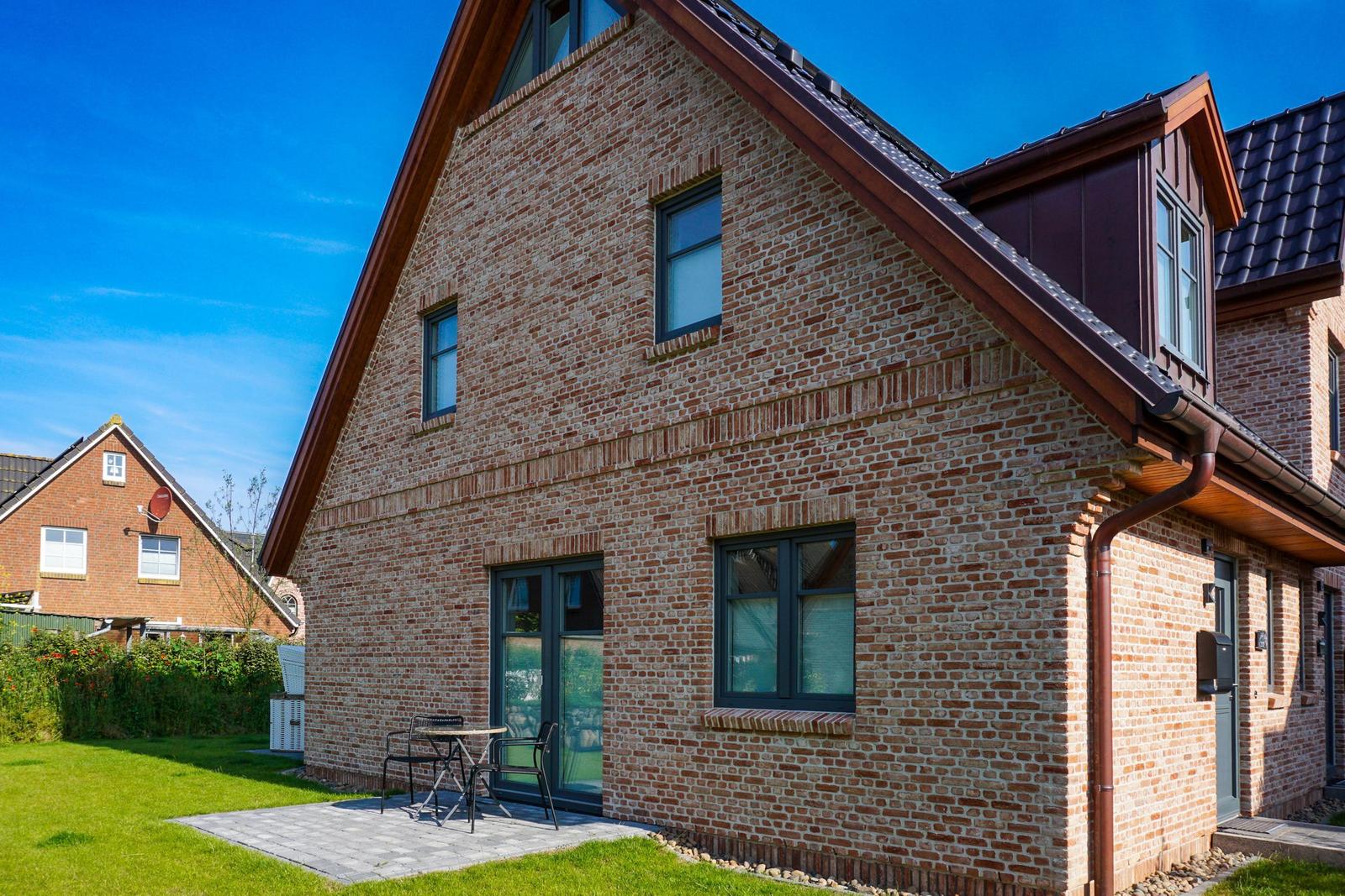 Ein zweistöckiges Haus mit Backsteinfassade und Terrasse mit Tisch und Stühlen.