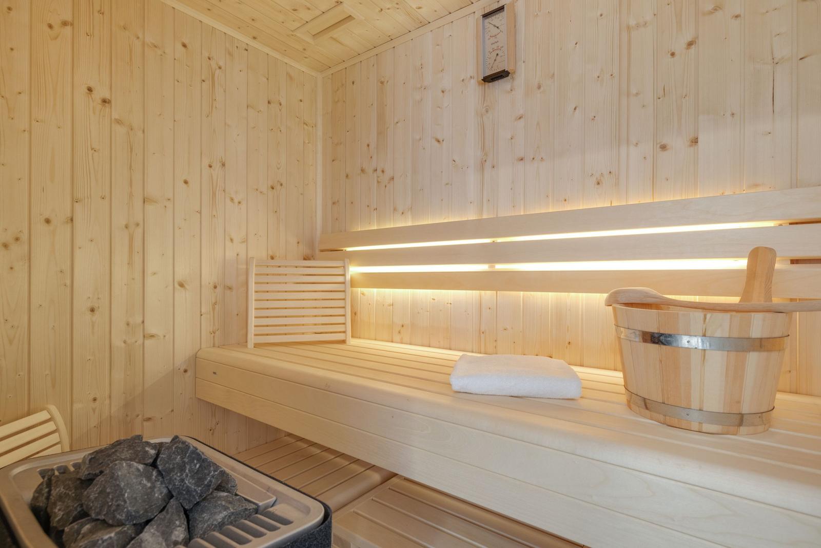 Sauna mit Holzbank, Thermometer und Eimer.
