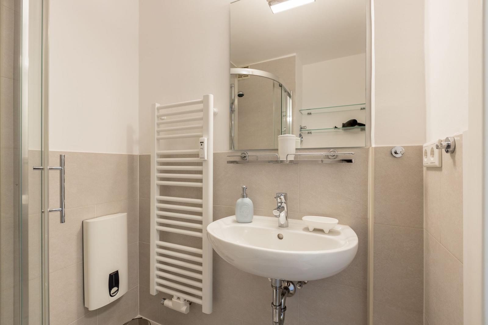Badezimmer mit Dusche, Waschbecken und Heizkörper