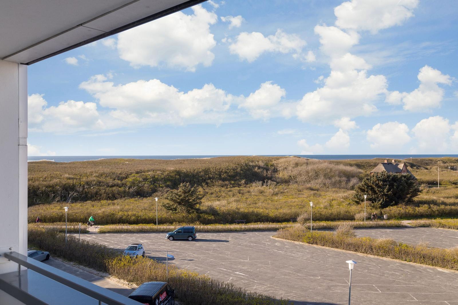 Blick von Balkon auf Parkplatz und Dünen mit Meer im Hintergrund.