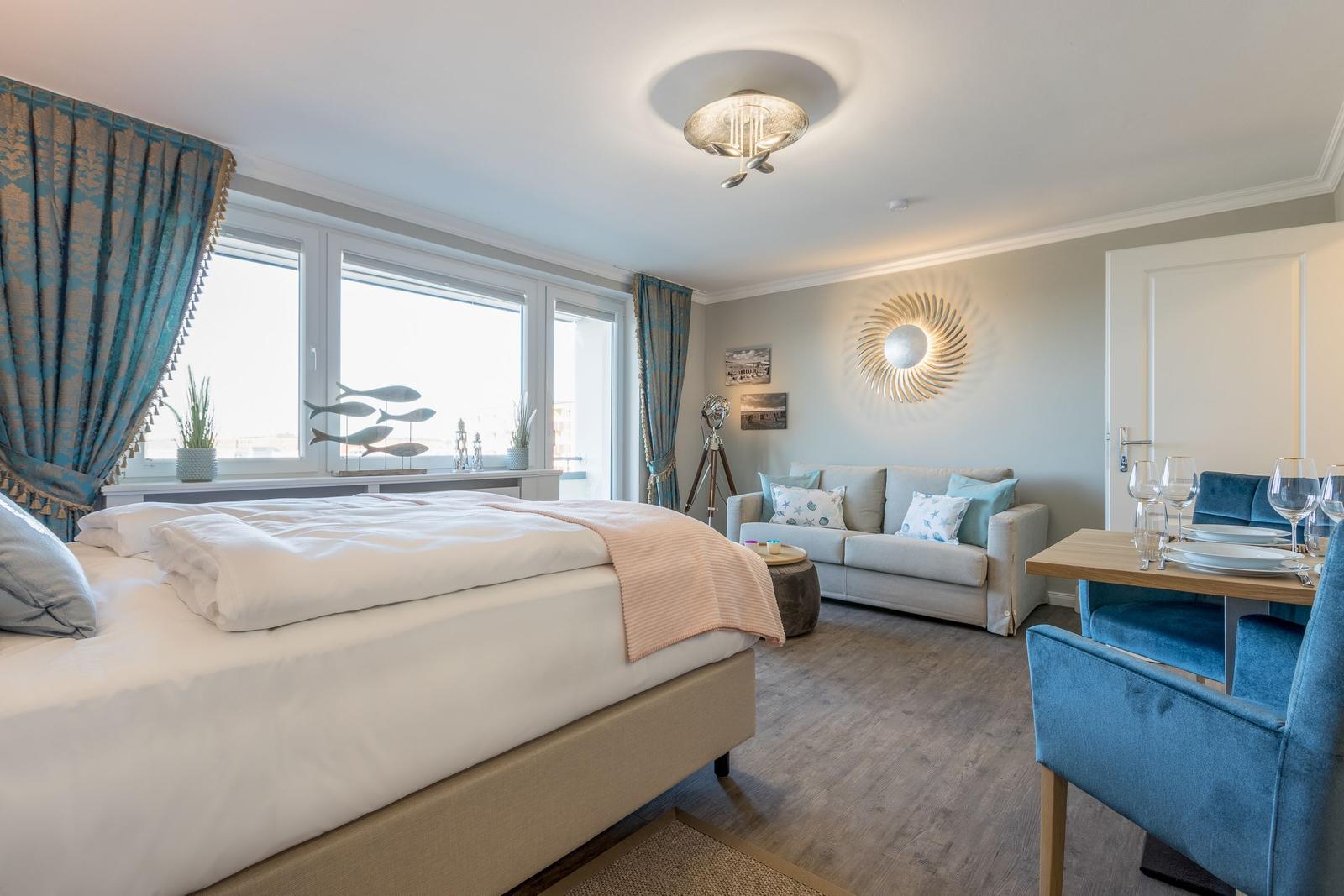Schlafzimmer mit Bett, Sofa und Esstisch. Blaue Vorhänge und Wanddekoration.