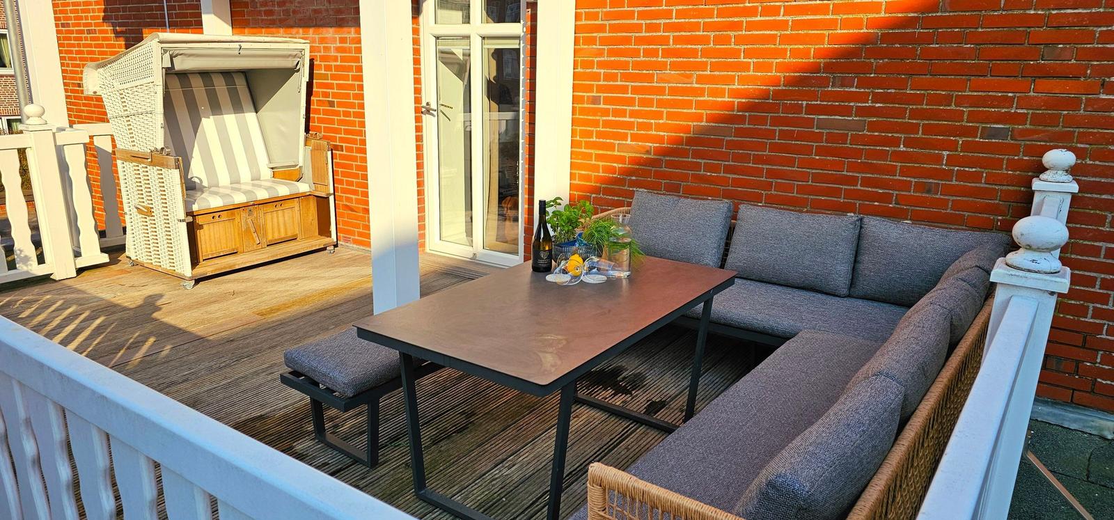 Terrasse mit Sitzgruppe, Tisch und Strandkorb vor rotem Backsteinhaus.