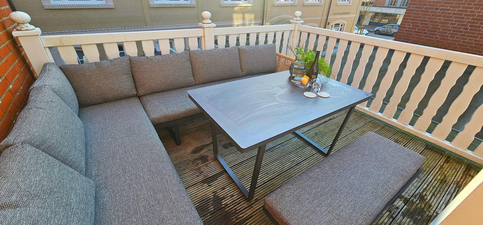 Terrasse mit Sitzgruppe und Tisch. Holzgeländer und Befestigung an Backsteinmauer.