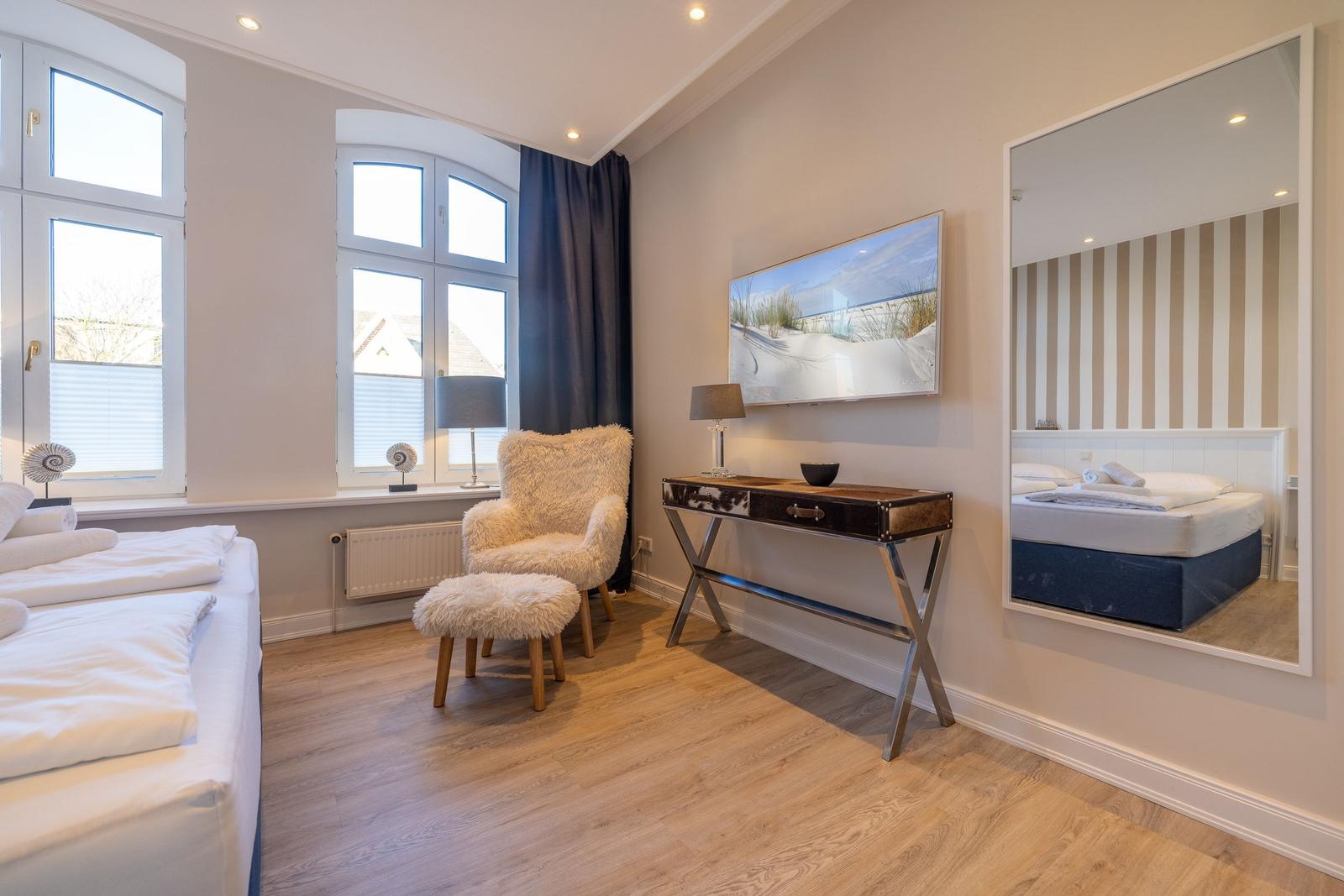 Schlafzimmer mit Bett, Stuhl, Schreibtisch und Spiegel.