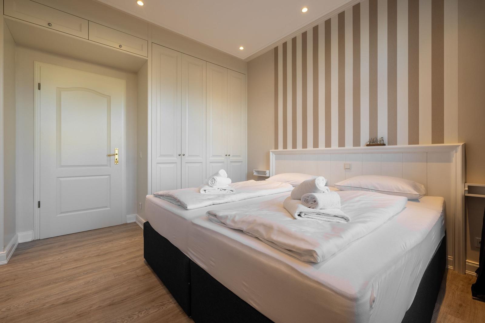 Schlafzimmer mit Doppelbett, Kleiderschrank und gestreifter Wand.