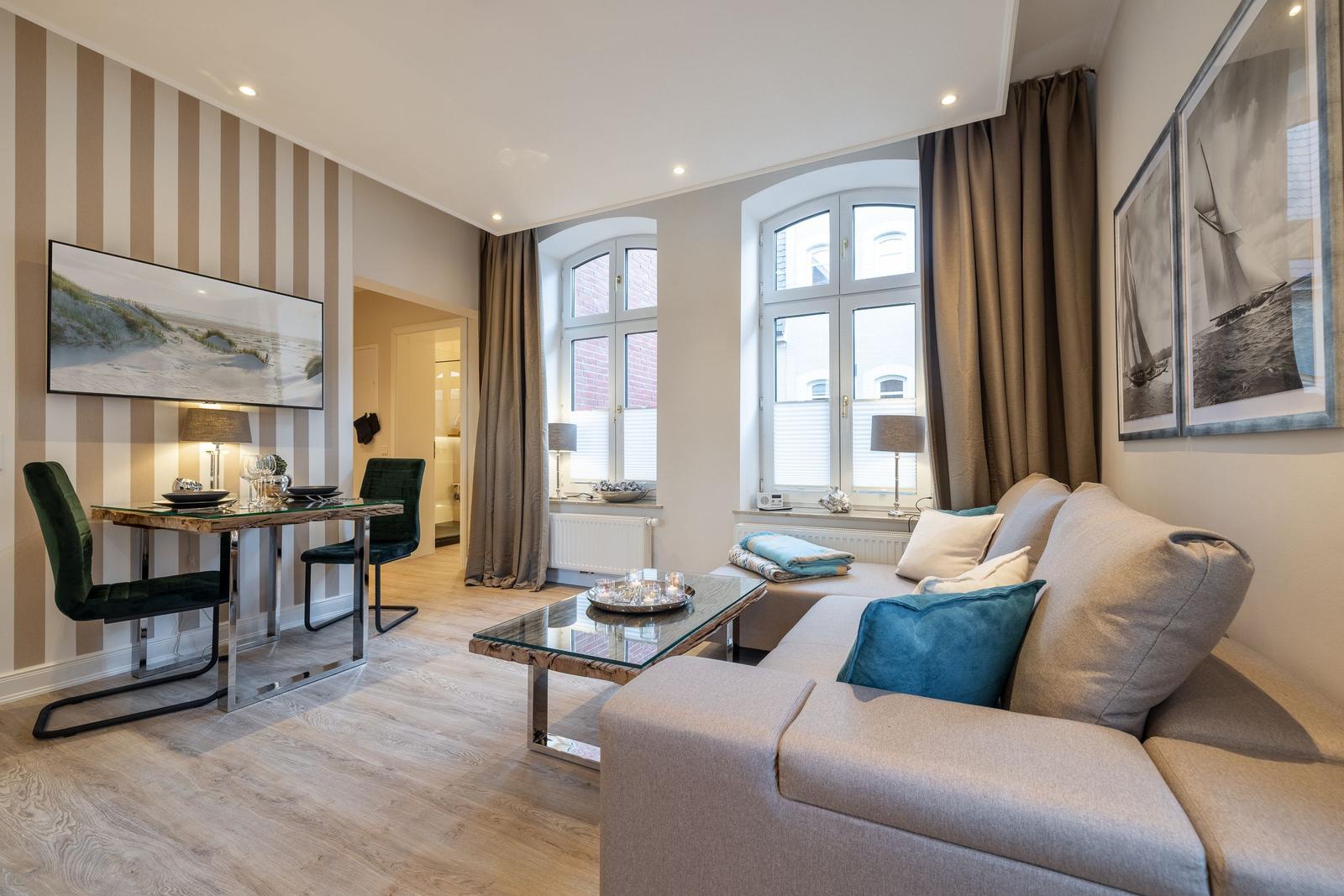 Wohnzimmer mit Sofa, Glas-Tisch und Fenstern mit Vorhängen.