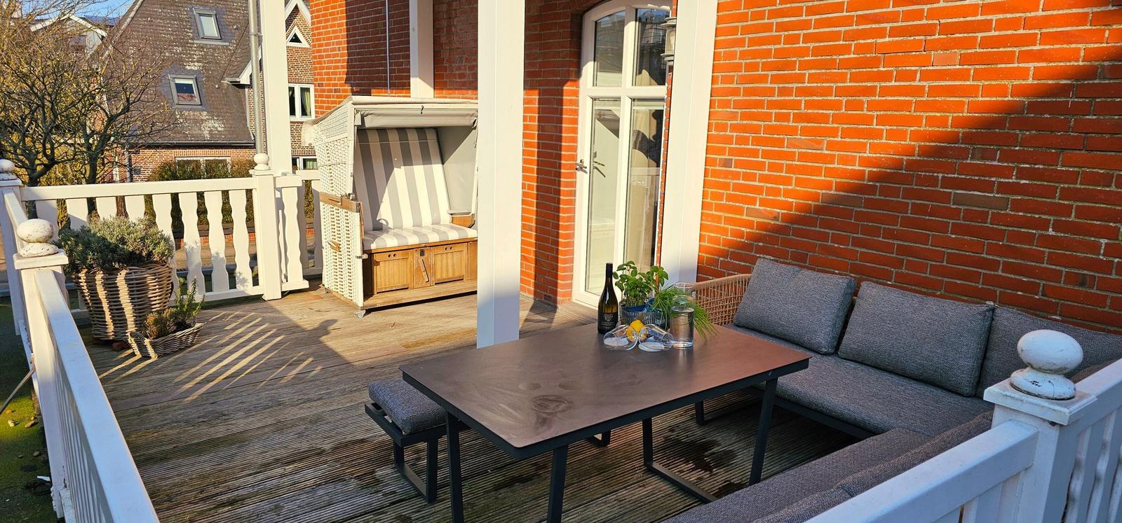 Terrasse mit Sitzgruppe, Tisch und Liegestuhl vor rotem Backsteinhaus.