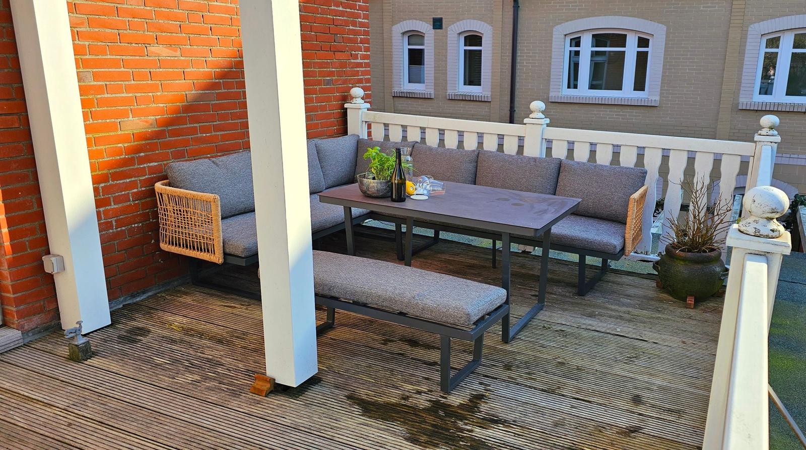 Terrasse mit Sitzgruppe, Tisch und Pflanzen an roter Backsteinwand.