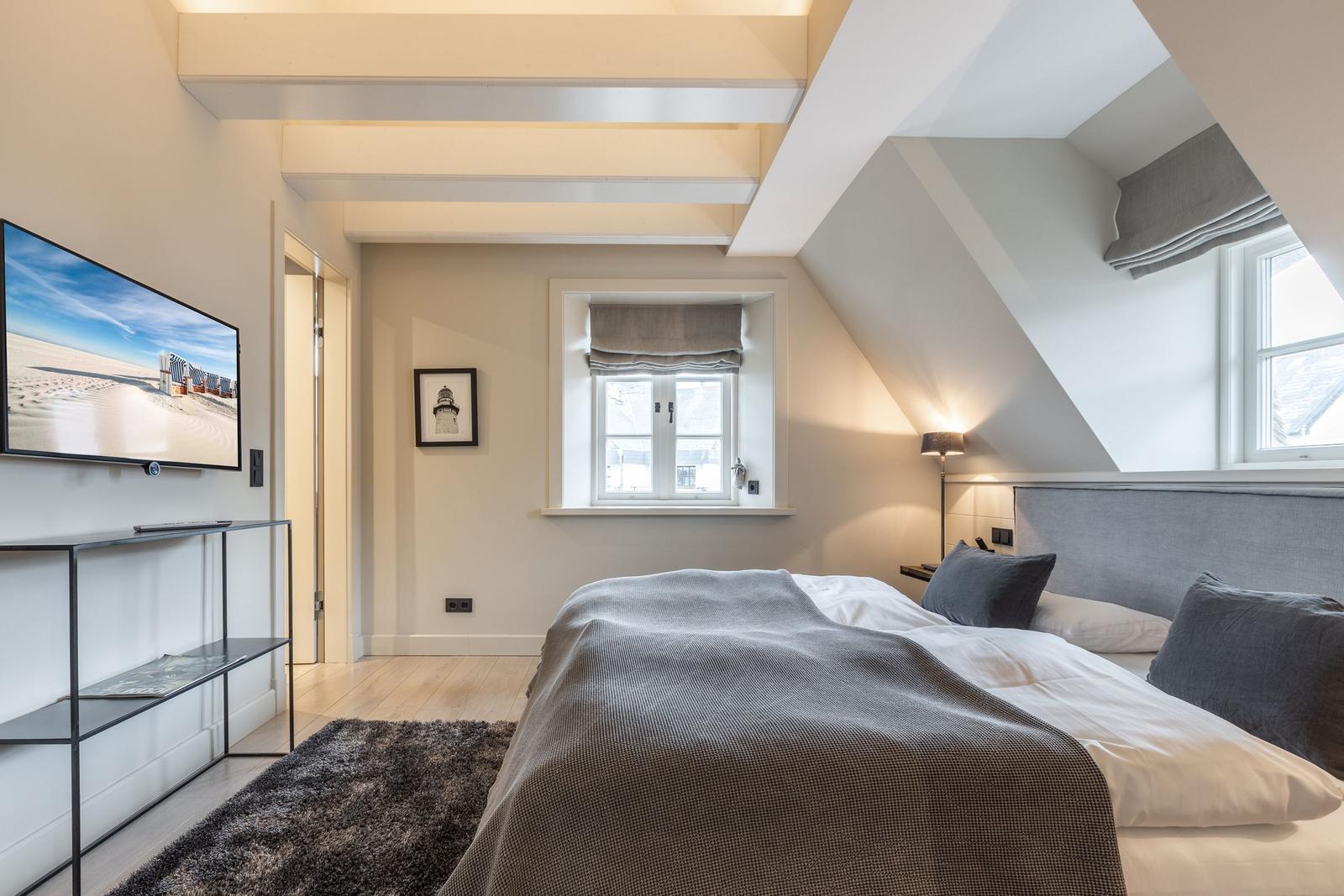 Schlafzimmer mit Dachschrägen, Bett, Fernseher und Fenster.
