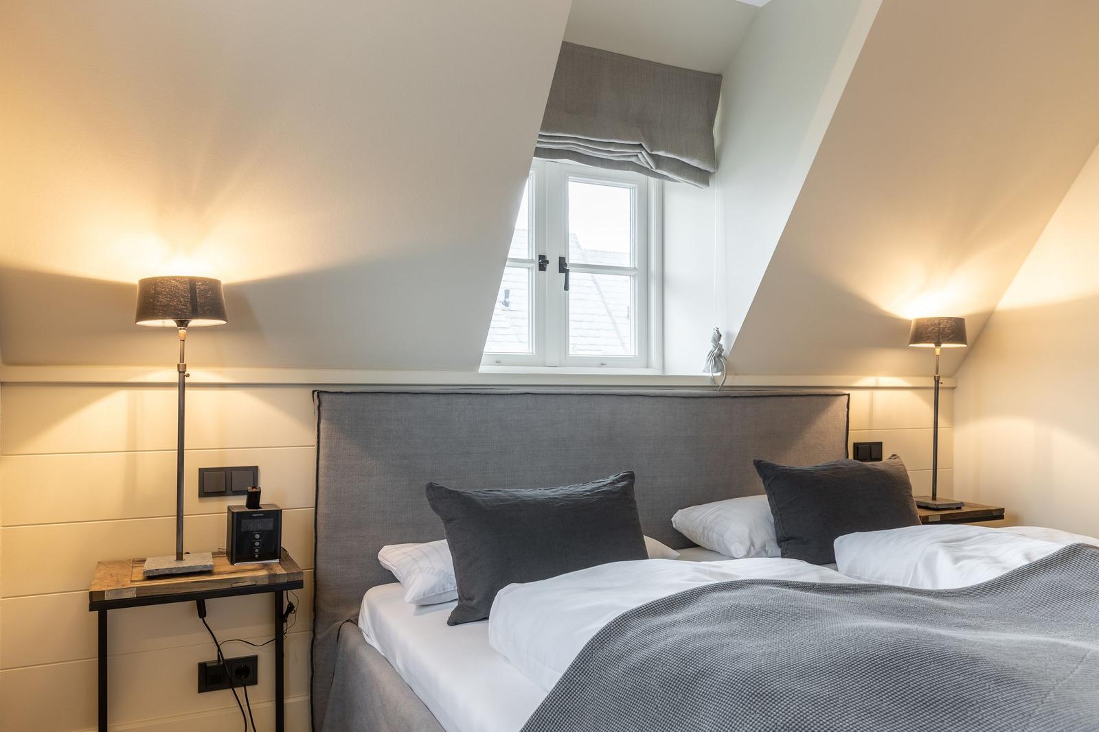 Schlafzimmer mit Dachschräge, Bett, zwei Nachttische und Fenster.