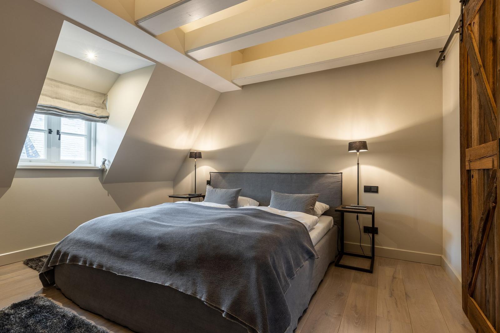 Schlafzimmer mit Dachschrägen, Bett, Nachttischen und Fenster.