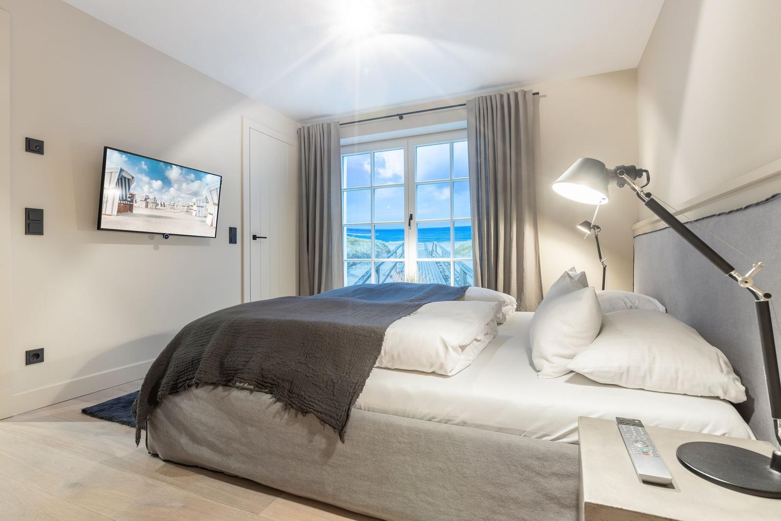 Schlafzimmer mit Blick aufs Meer, großes Bett, TV und Stehlampe.