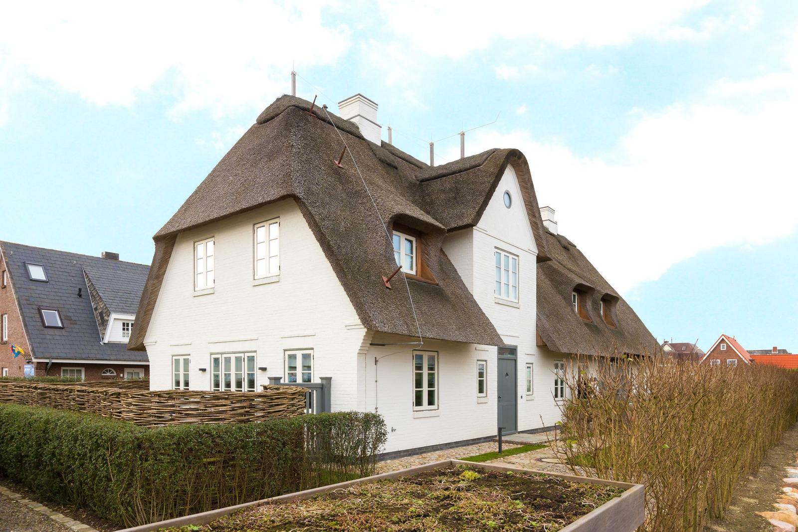 Weiße Hütte mit strohgedecktem Dach und Fenstern.