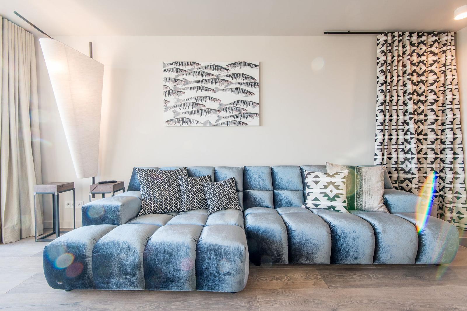 Ein Wohnzimmer mit einem blauen Sofa, Kissen und einem Wandbild mit Fischen.