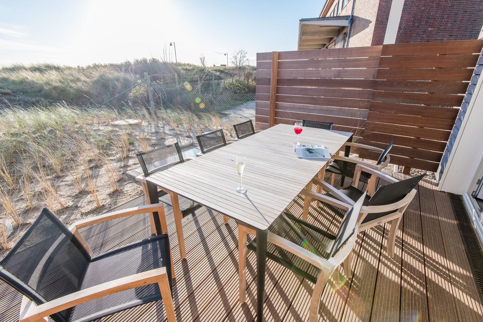 Terrasse mit Tisch und Stühlen, Blick auf Dünen.