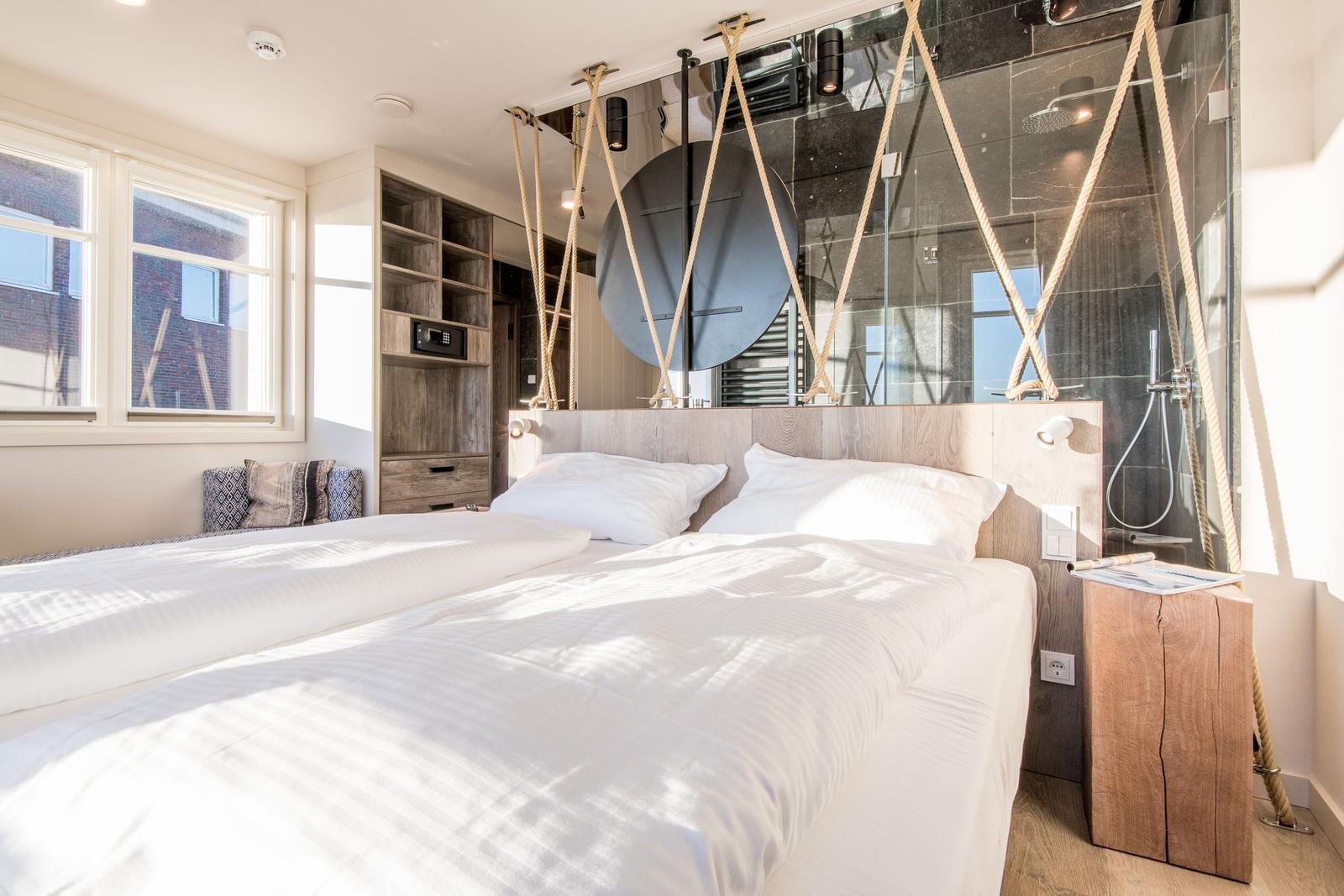Schlafzimmer mit Bett, Holzmöbel und Dusche im Hintergrund.