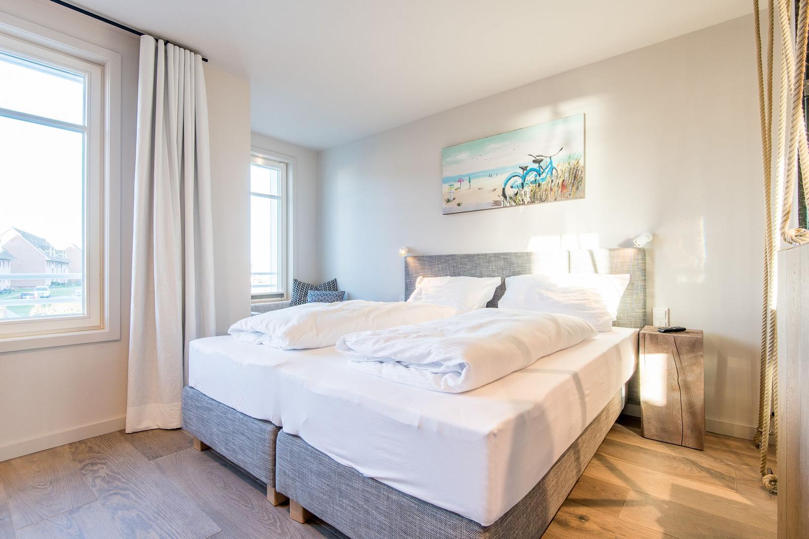 Schlafzimmer mit Doppelbett, Fenstern und Wandbild.