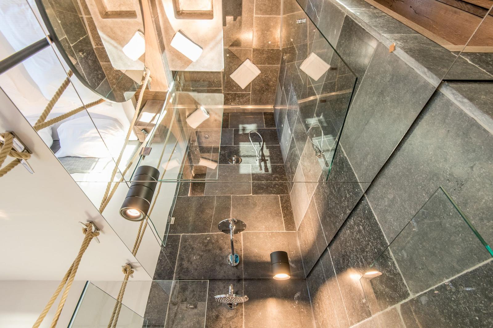 Dusche mit Glaswand, dunklen Fliesen und modernen Lichtern.
