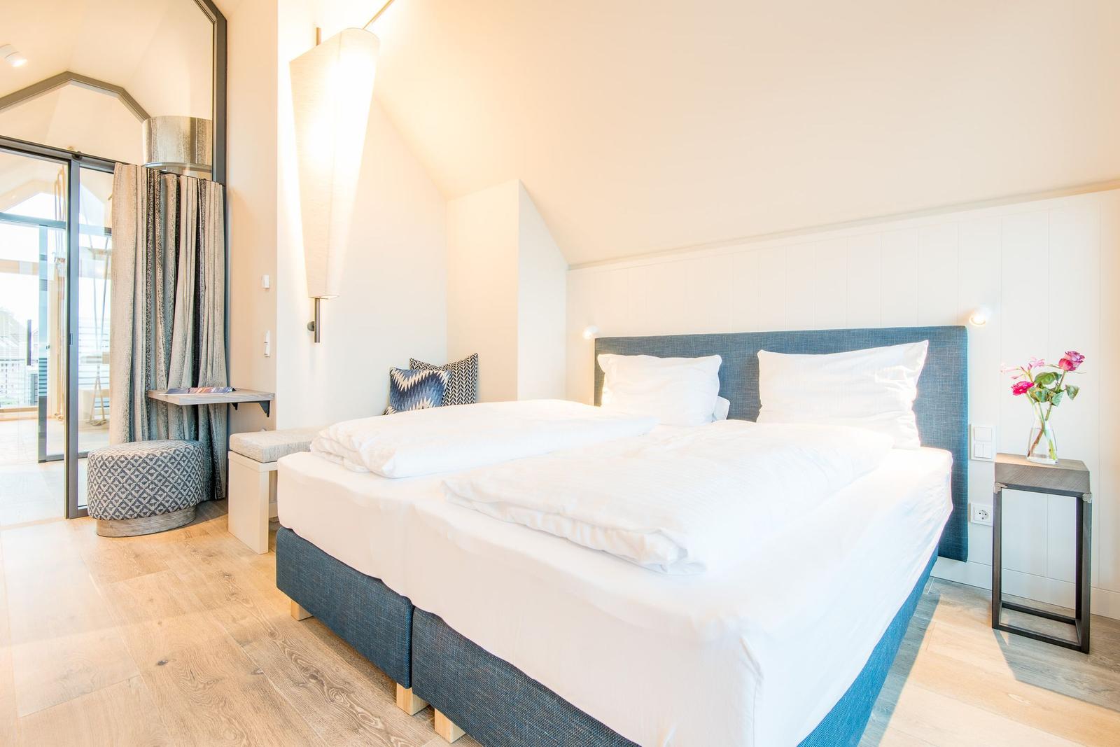 Schlafzimmer mit Doppelbett, Nachttisch und Blick auf Balkon.