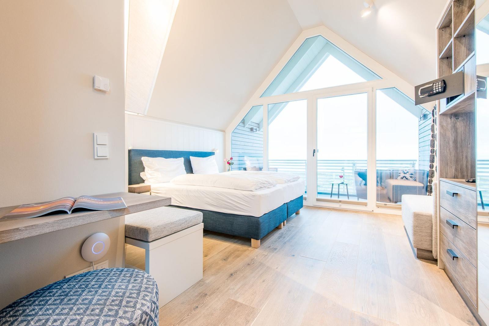 Schlafzimmer mit Balkon, Bett, Schreibtisch und Holzboden.