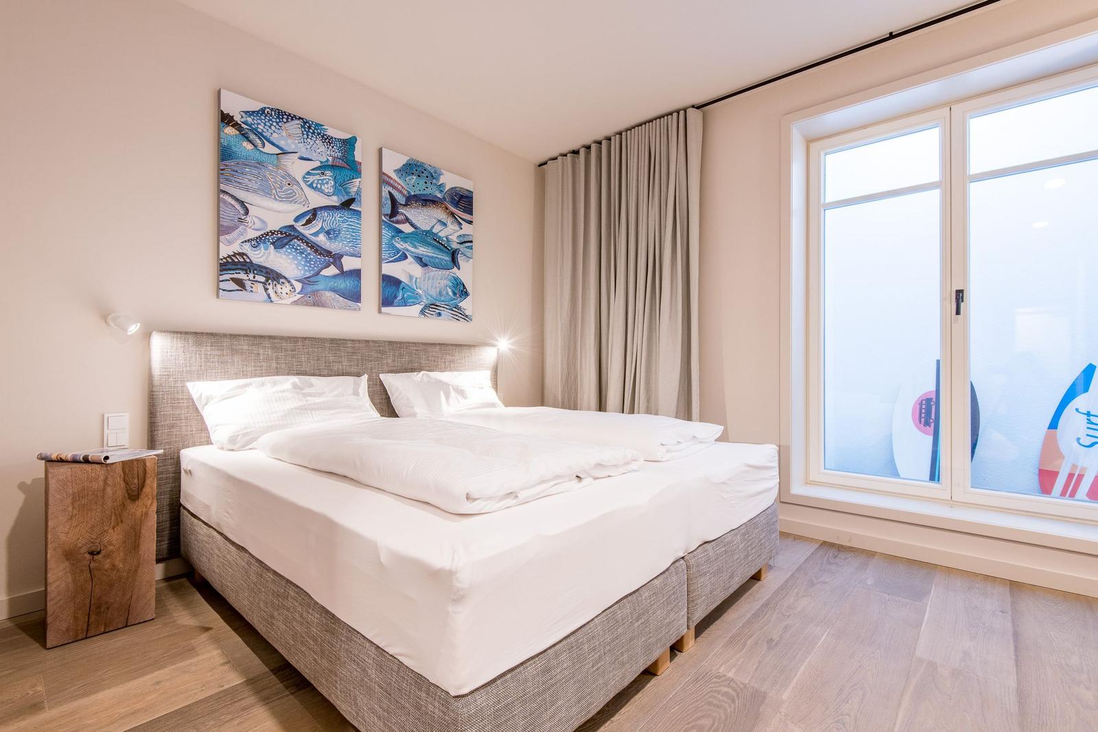 Schlafzimmer mit Doppelbett, Wandbildern und großem Fenster.