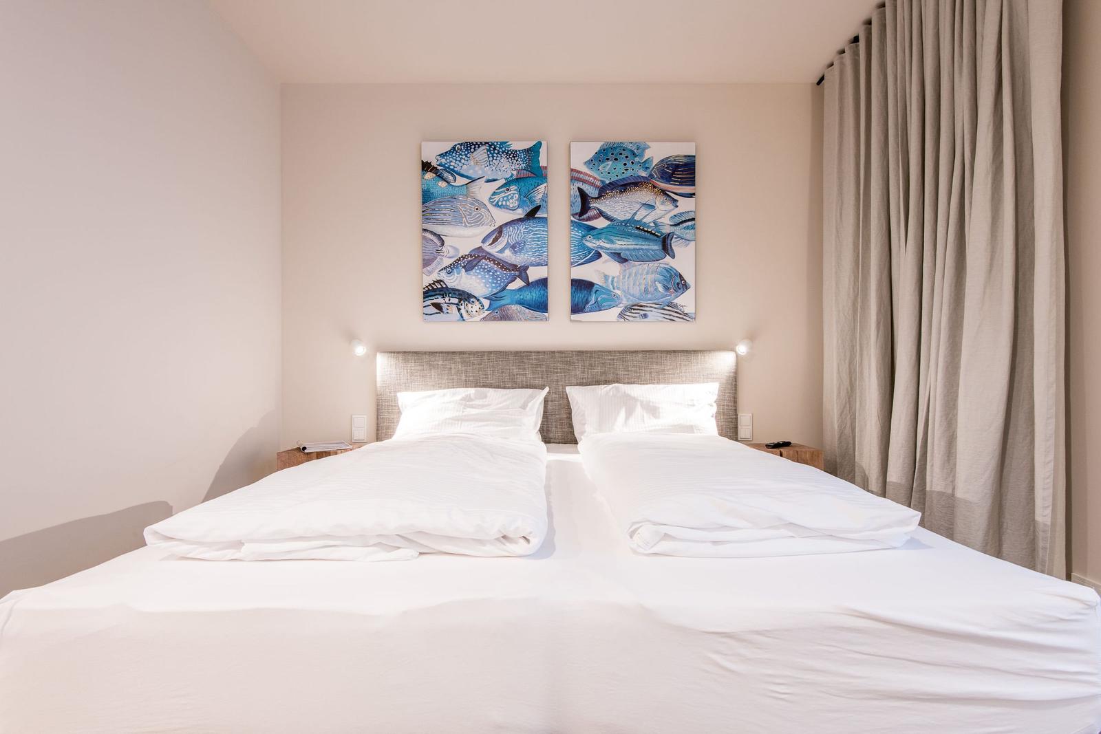 Schlafzimmer mit Doppelbett, Wandbildern und Vorhängen.
