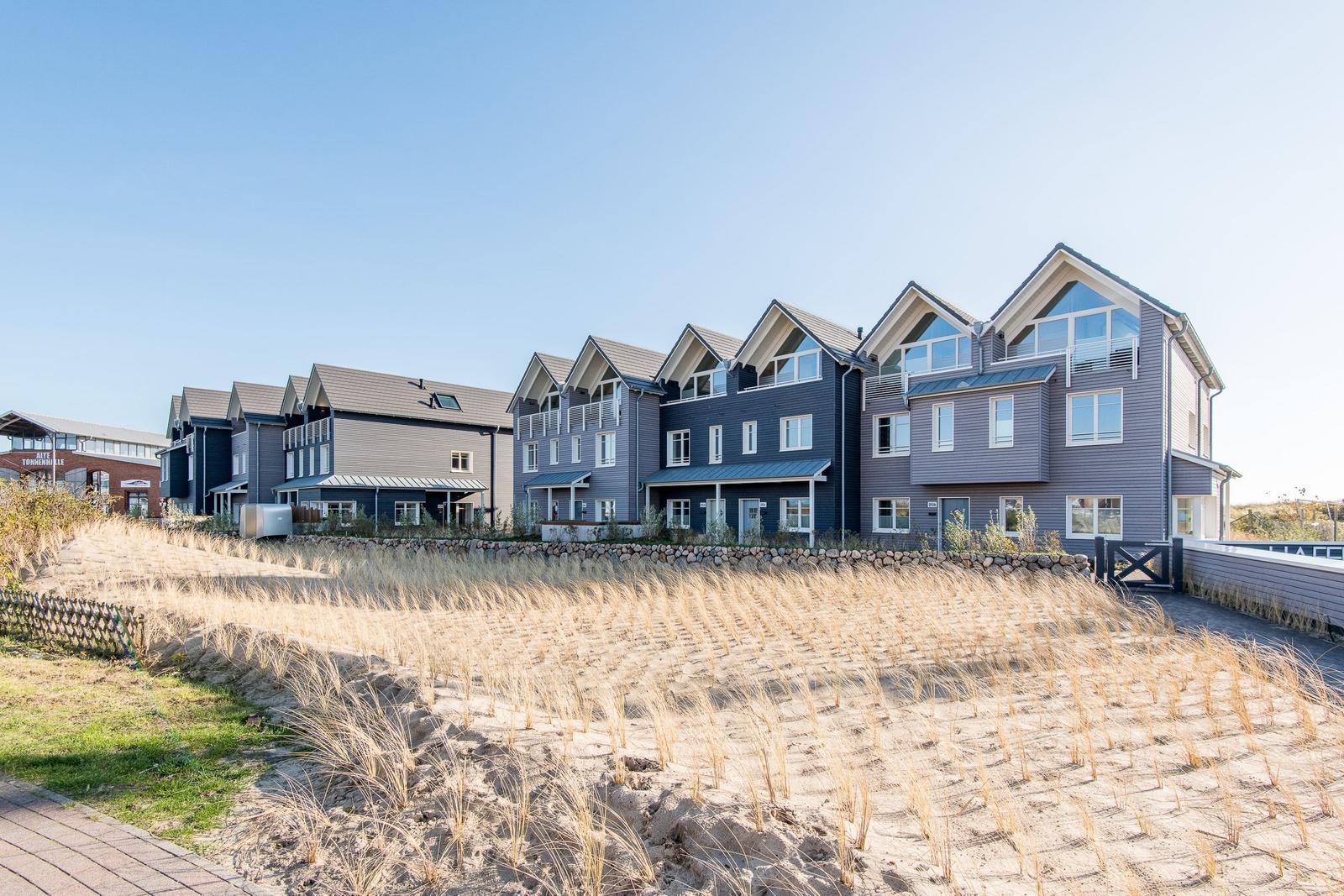 Moderne Ferienhäuser mit Balkonen und großen Fenstern an einem sandigen Strand.