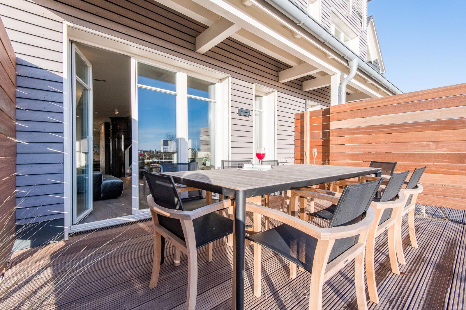 Terrasse mit Tisch und Stühlen, Blick ins Haus, Holzverkleidung und Sichtschutzwand.