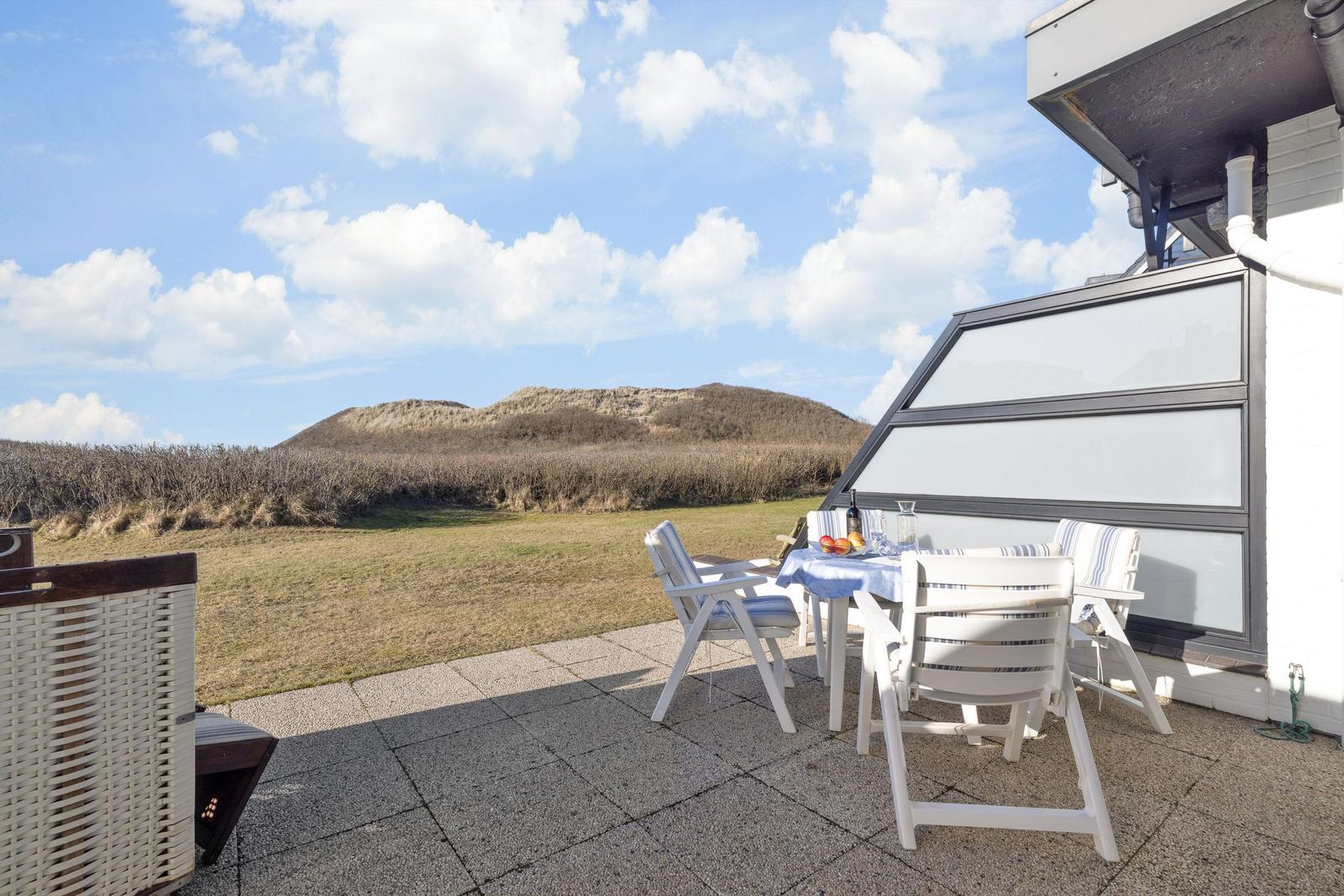 Terrace with table and chairs, view of dunes and sky.