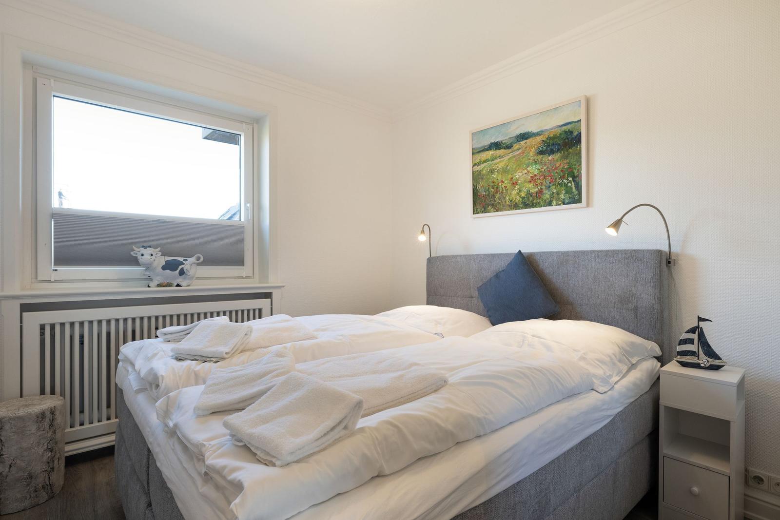 Bedroom with bed, window, nightstand, and wall picture.
