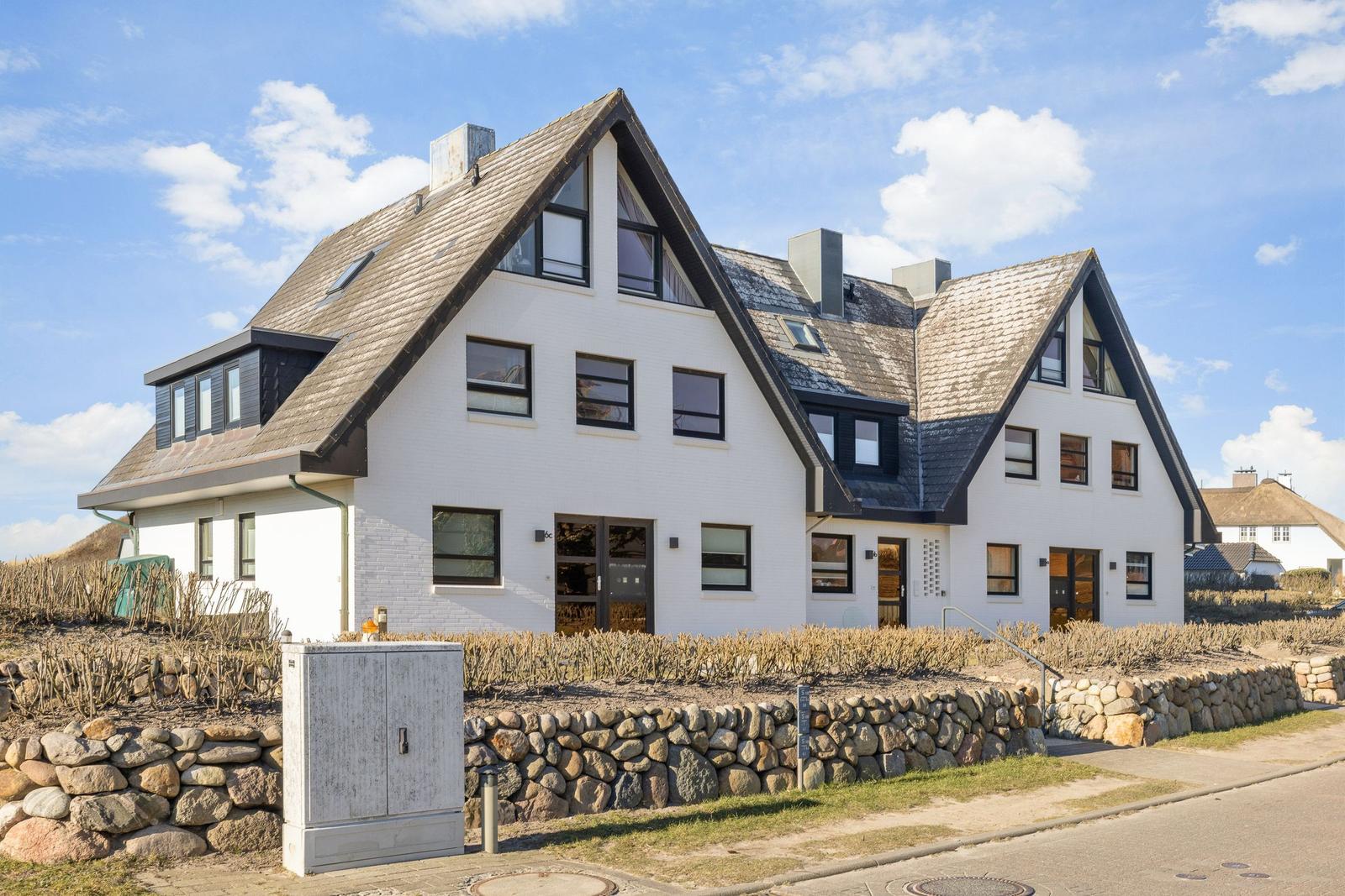 House with white walls and dark window frames under a blue sky.