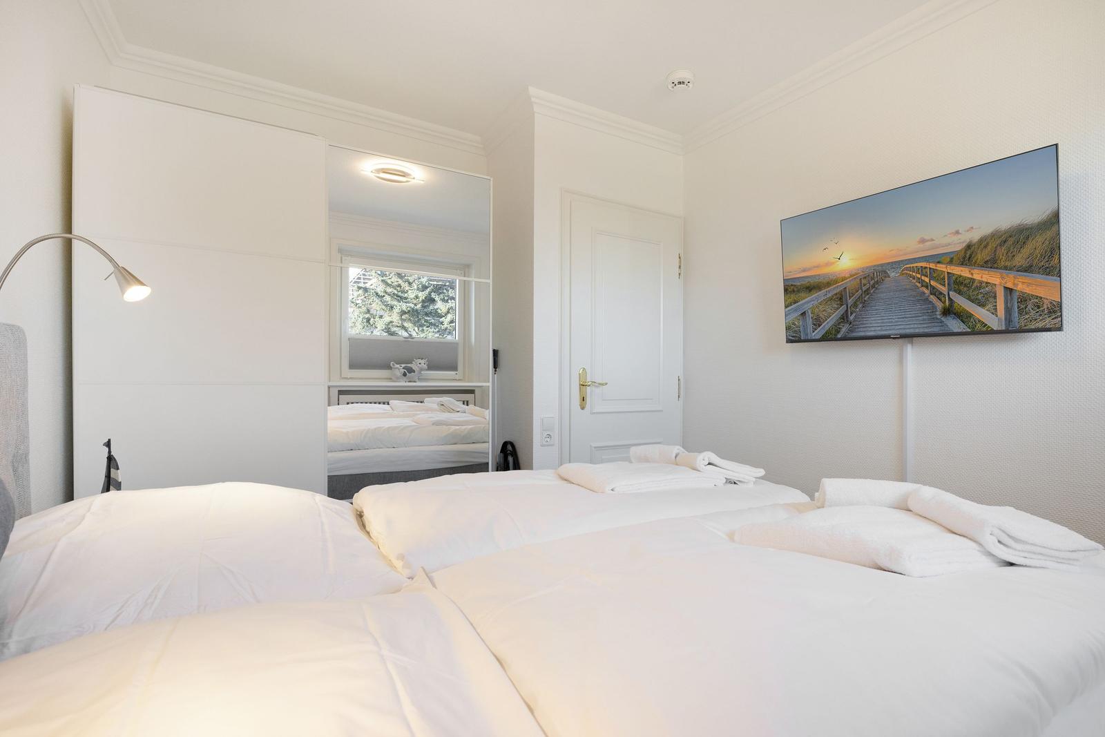 Room with double bed, mirror, and wall picture. White walls and ceiling.