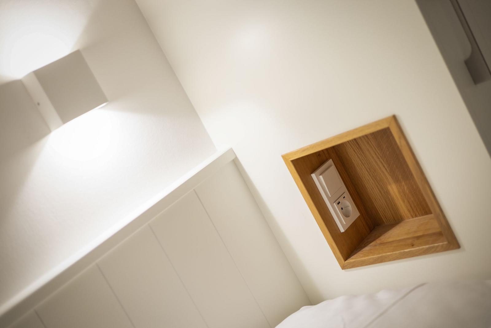 Wall with wooden frame and socket next to bed and wall lamp