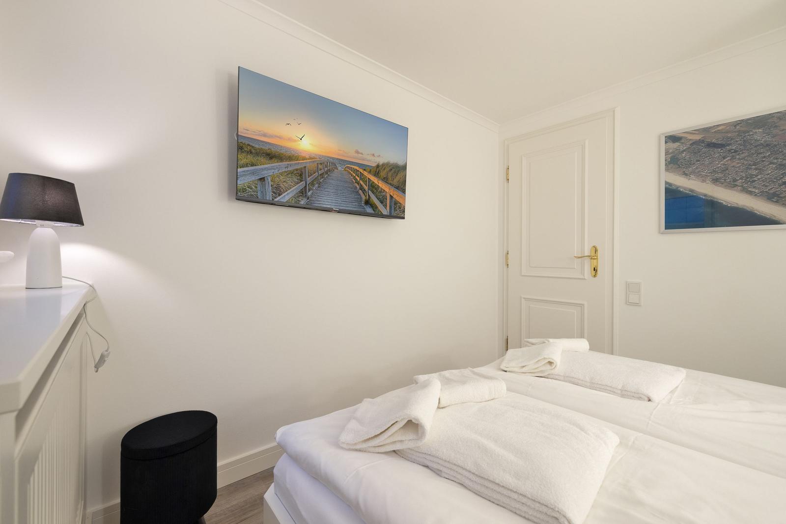 Bedroom with bed, towels, and wall art. Door and nightstand visible.