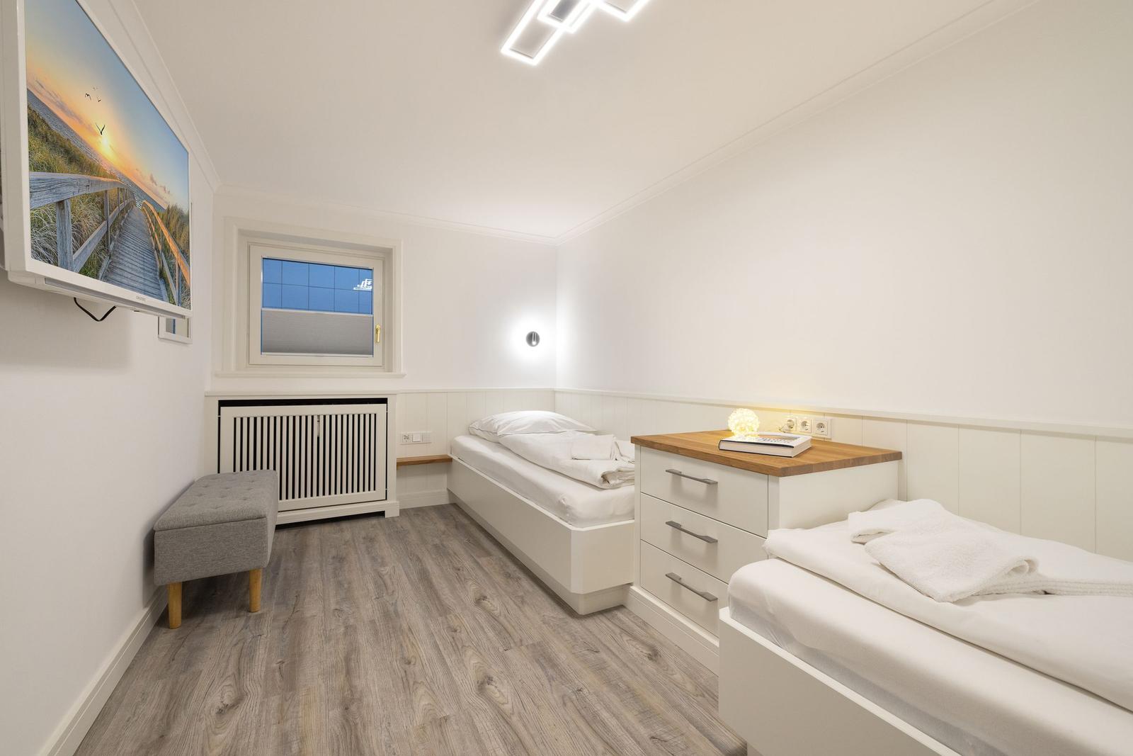 Room with two beds, wardrobe and window. Wall picture and wooden floor.