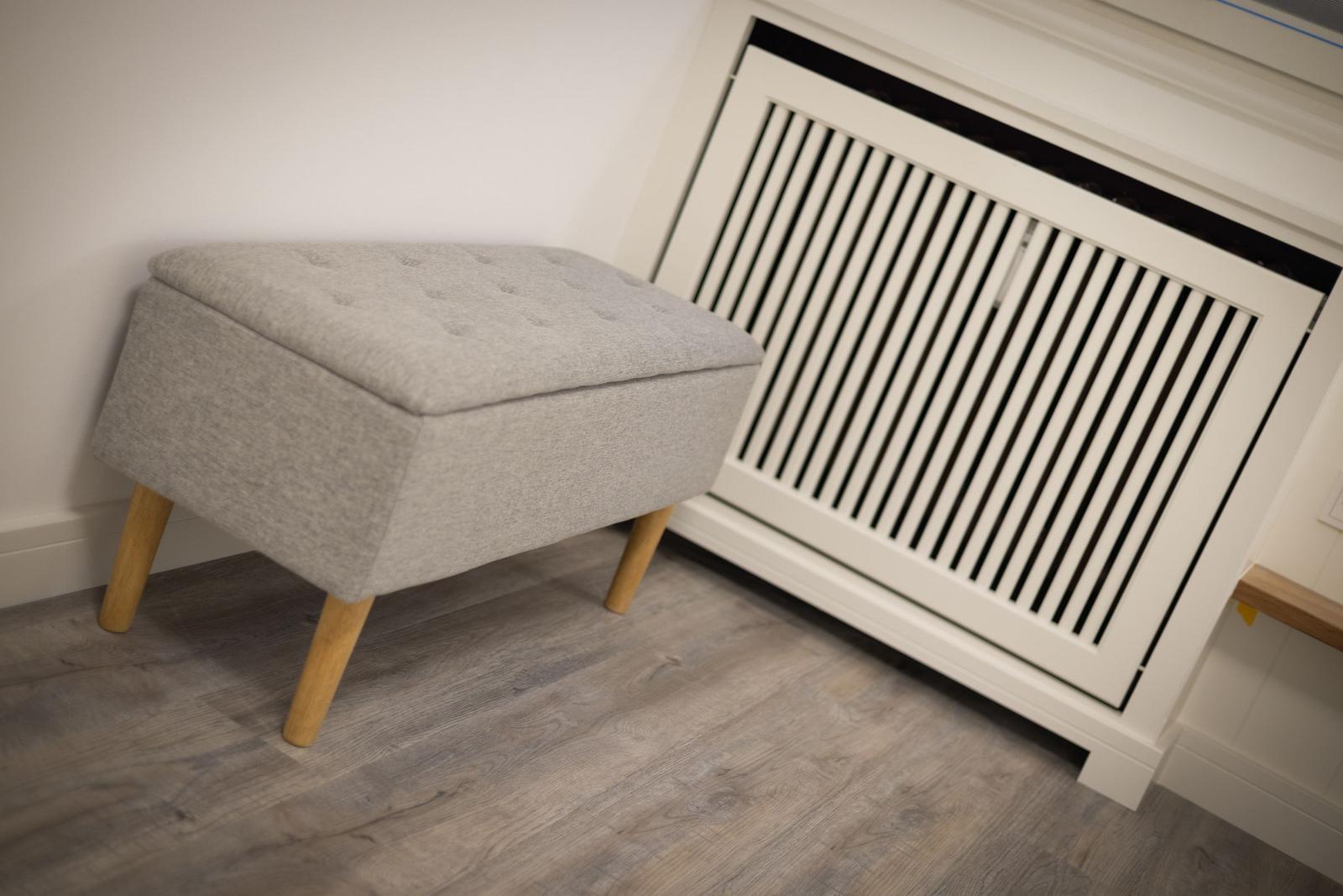 Gray ottoman with wooden legs next to heater