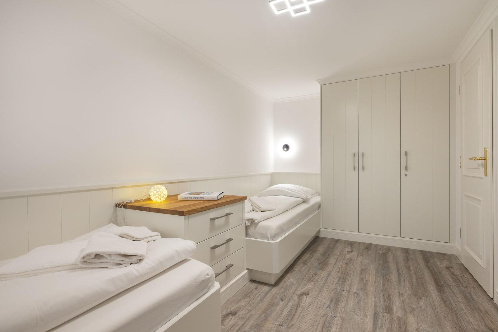 Room with two beds, wardrobe, and wooden floor.