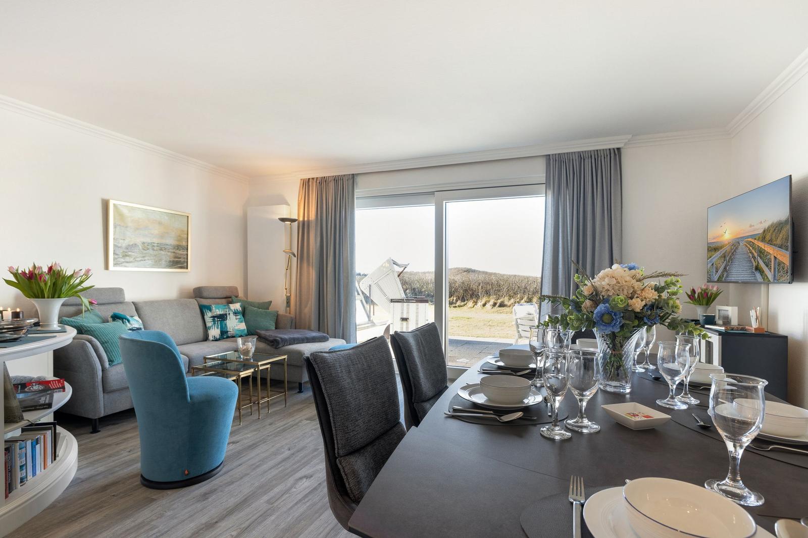 Dining area with table and chairs, living area with sofa and armchair, view of terrace and landscape.