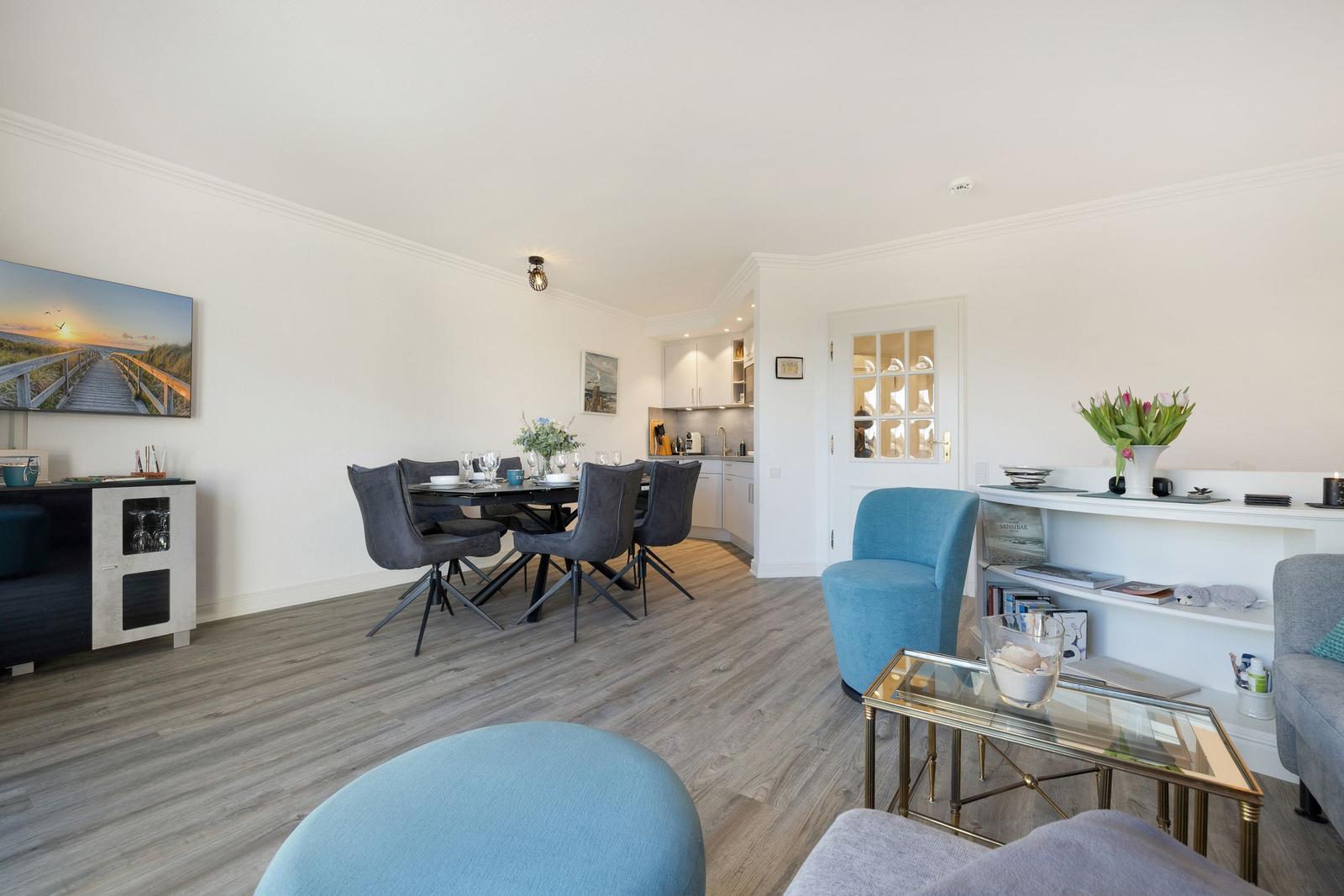 Living and dining area with dining table, blue chairs, and kitchen area.