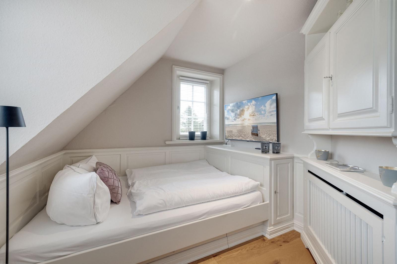 Schlafzimmer mit Dachschräge, Bett, Fenster und Fernseher.