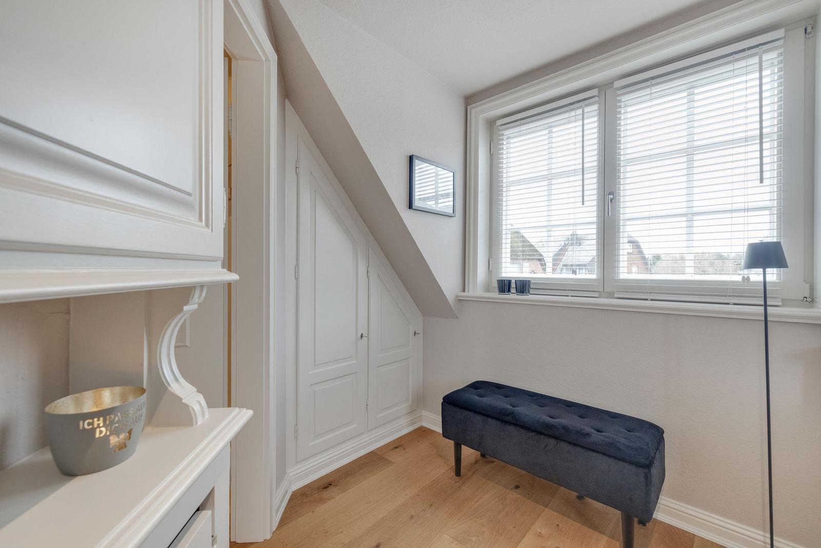 Ein Raum mit Dachschräge, Fenster mit Jalousien, blauer Sitzbank und weißer Einbauschränke.
