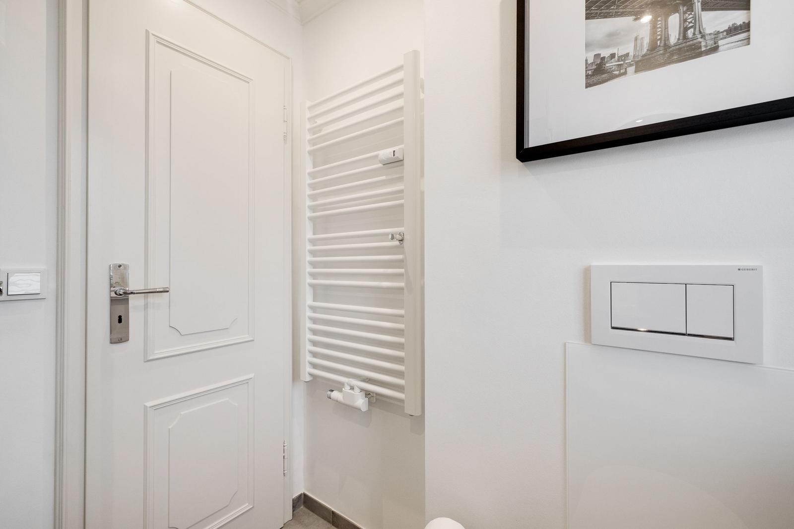 Helle Toilette mit Heizkörper, Spiegel und Bild an der Wand.