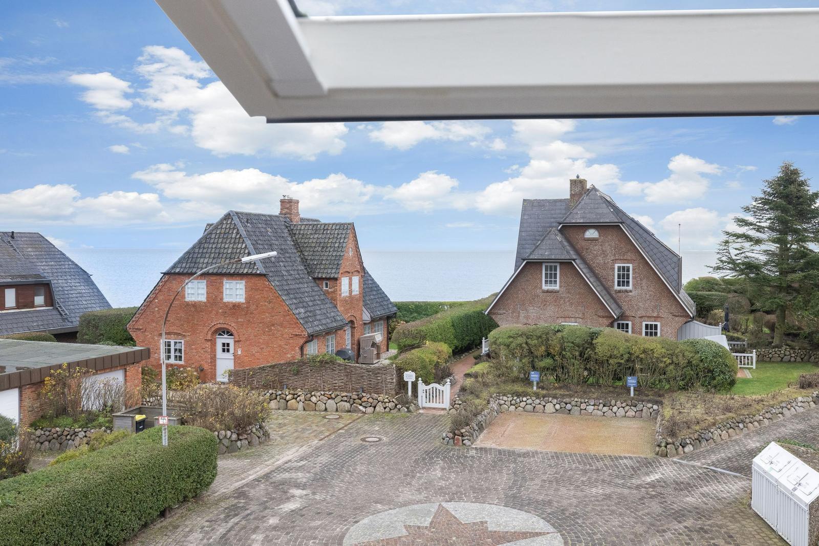Roter Backsteinhaus mit grauem Dach, umgeben von Grünflächen und Steinmauern.