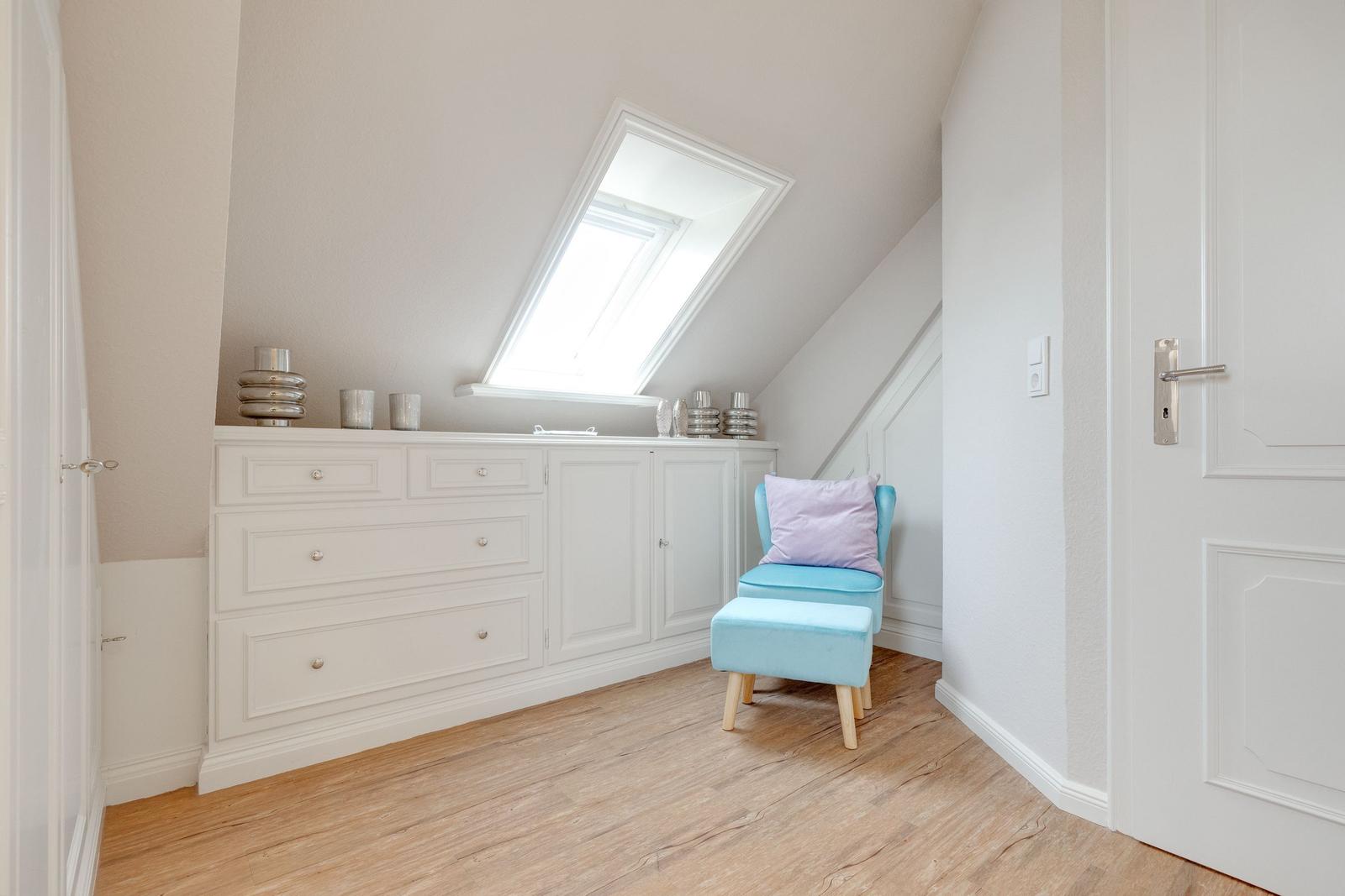 Schlafzimmer mit Dachschrägen, weißem Schrank und blauem Sessel.