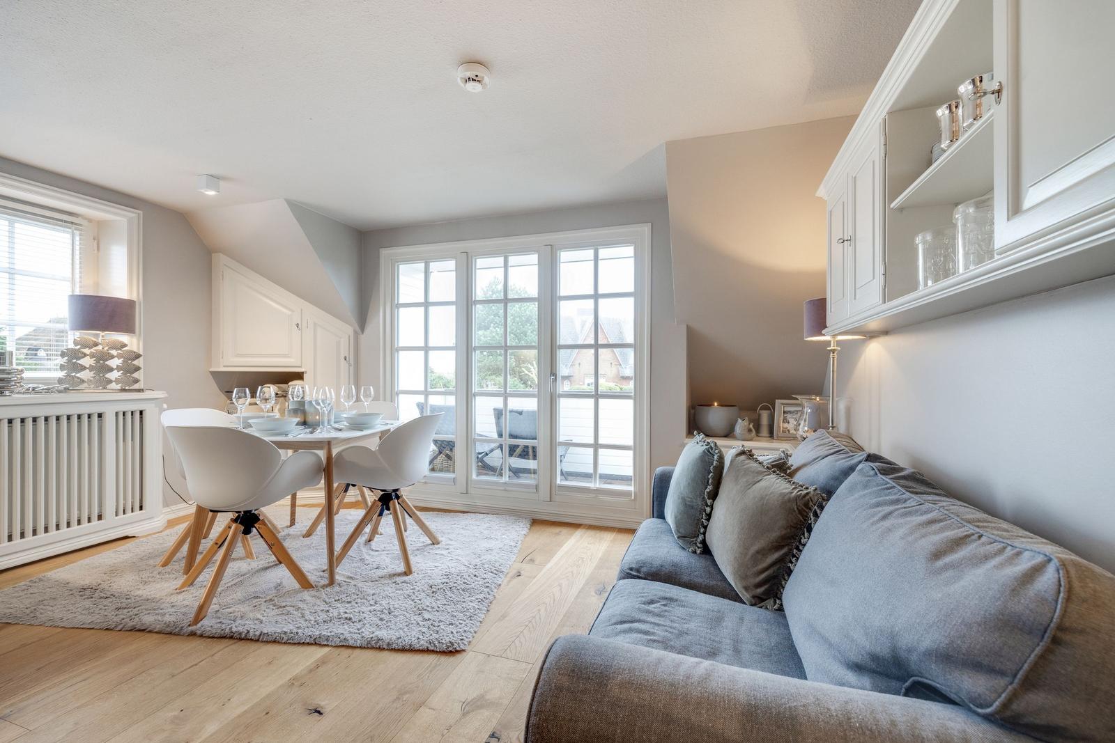 Wohn- und Essbereich mit Sofa, Tisch und Stühlen, Blick auf Balkon.