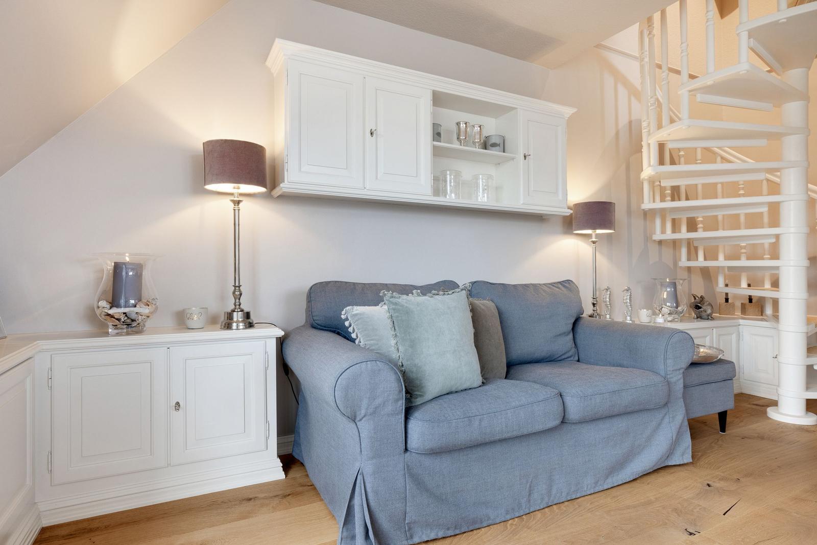Ein Wohnzimmer mit blauem Sofa, weißen Schränken und einer weißen Wendeltreppe.