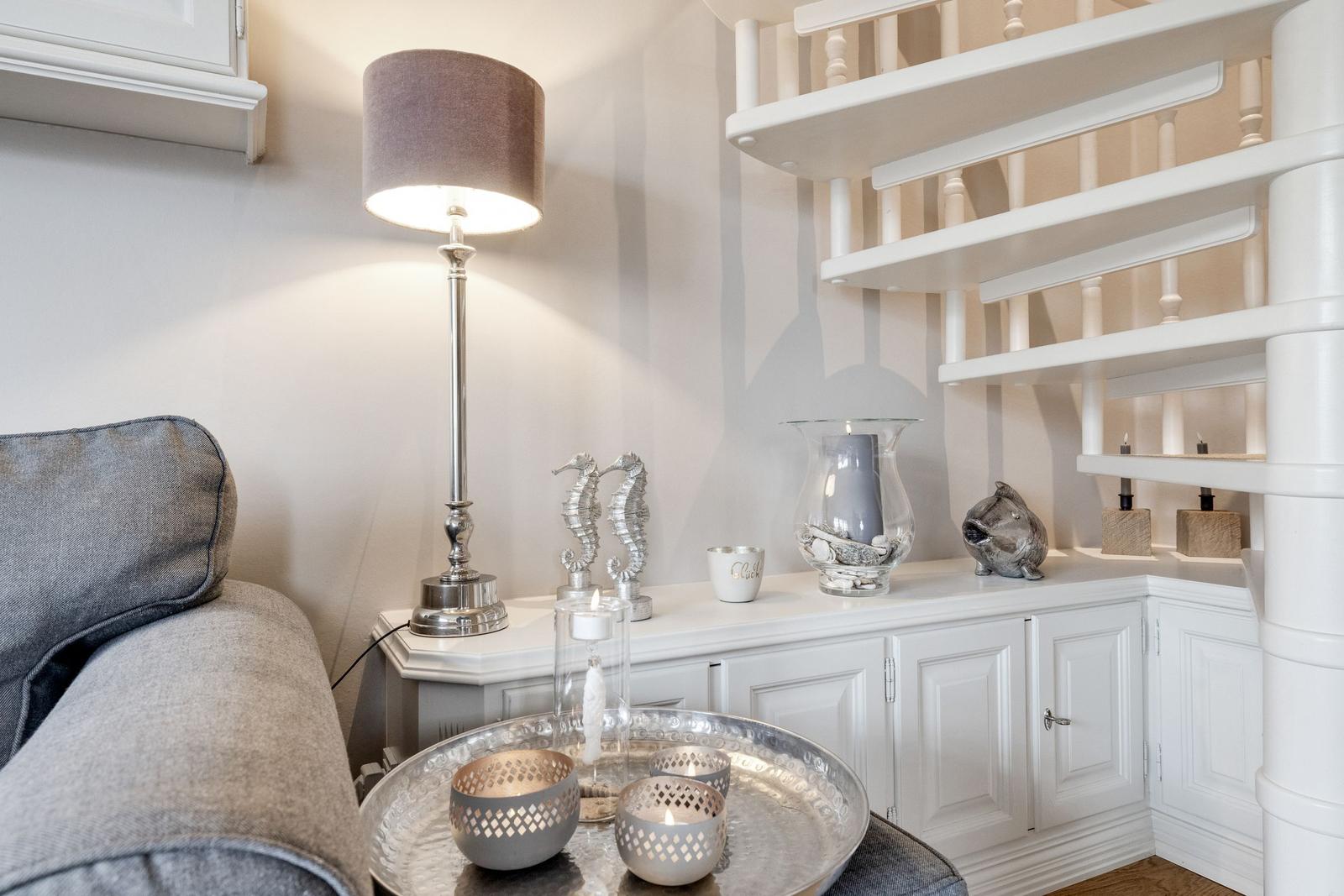 Ein Wohnbereich mit grauem Sofa, weißem Sideboard und einer Treppe.