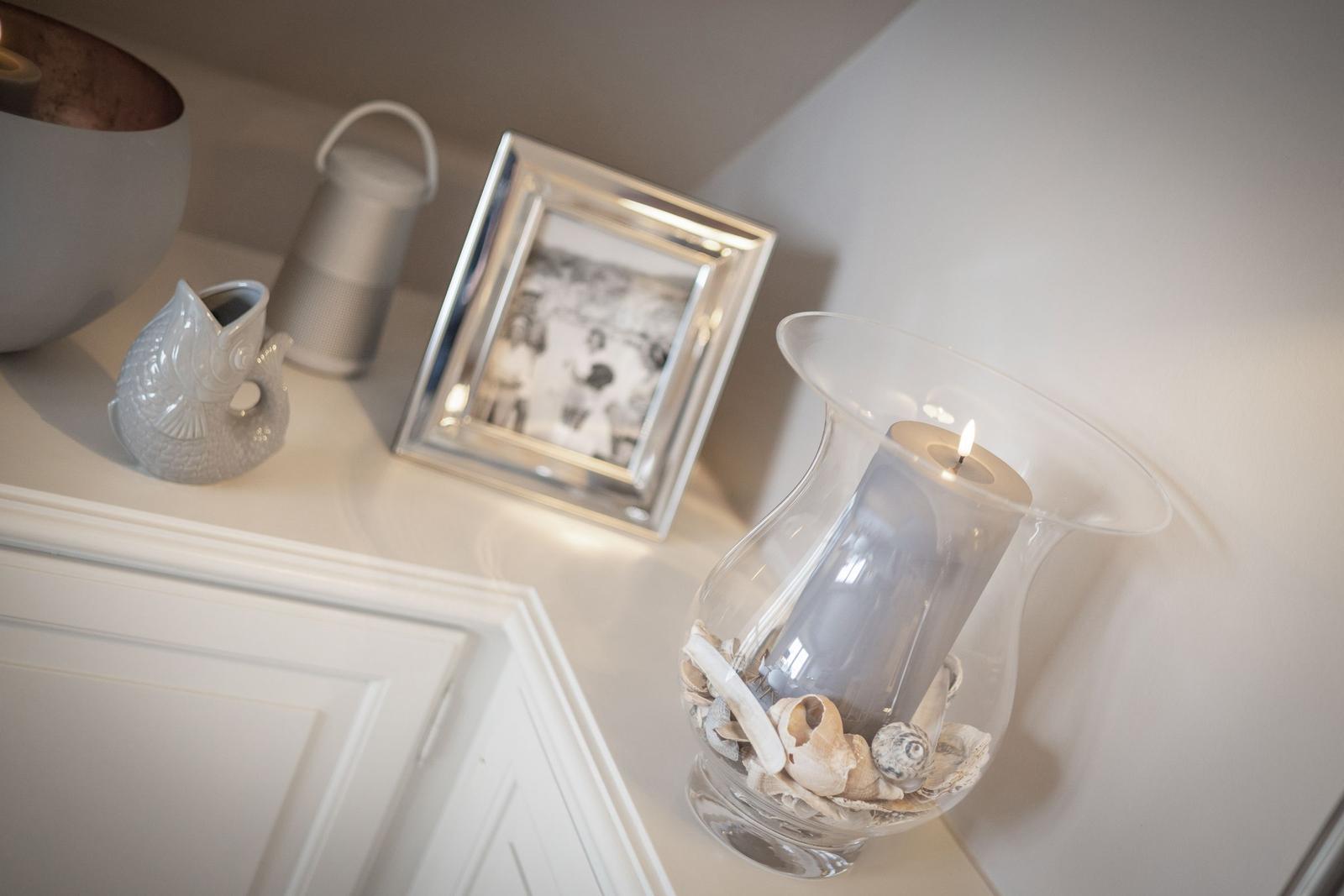 Auf einem Schrank stehen ein Bilderrahmen, eine Kerze und Meeresmuscheln.